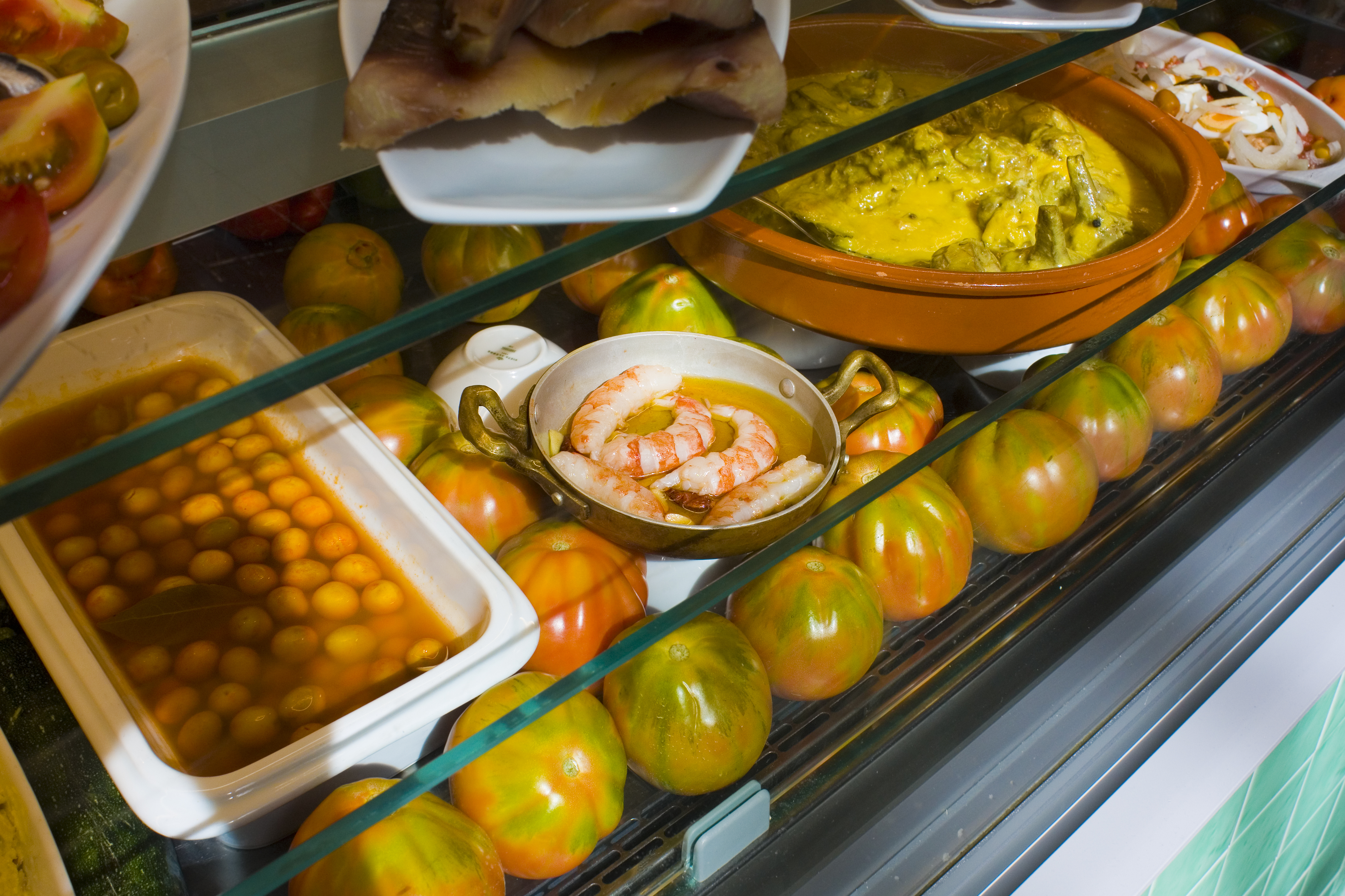 A tapas bar counter with tomatoes, prawns, olives and prepared dishes, reflecting Murcia&rsquo;s mix of huerta produce and seafood.